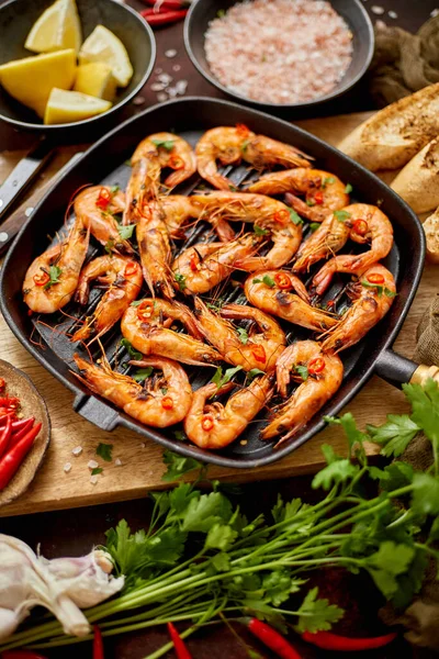 Roasted tiger prawns on iron grilling pan with fresh persley, lemon, chilli and bread