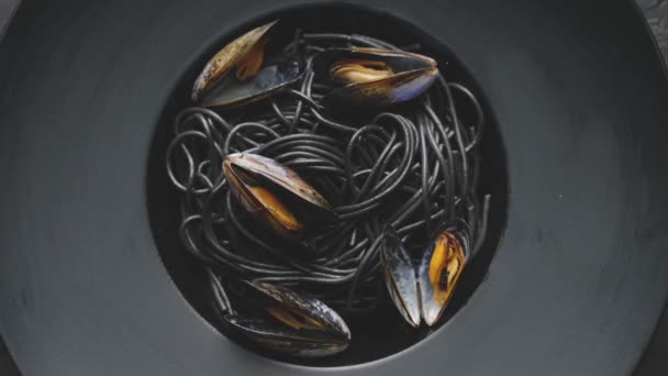Gros plan de délicieuses pâtes spaghetti noires servies avec des moules dans une assiette sombre — Video