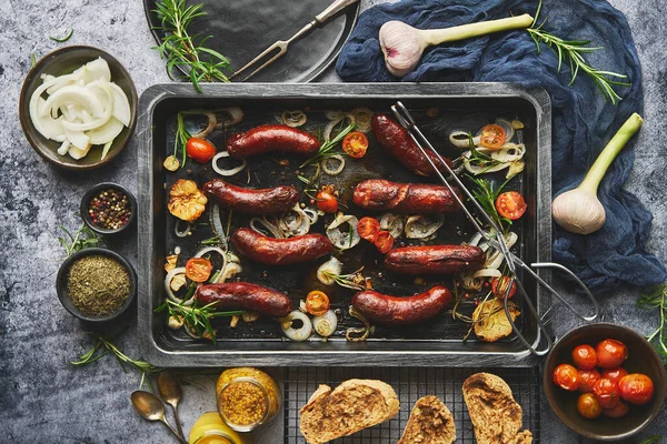 Vue de dessus sur de délicieuses saucisses grillées servies avec oignon, tomates, ail, pain et herbes — Photo