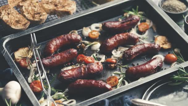 Sabrosas salchichas de romero caseras a la parrilla colocadas en bandeja de hierro sobre una mesa rústica de piedra oscura — Vídeos de Stock