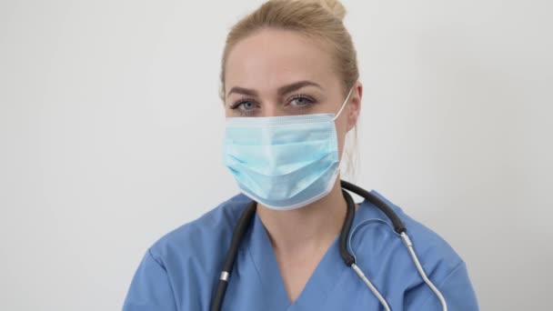 Женщина-врач в маске смотрит в камеру — стоковое видео