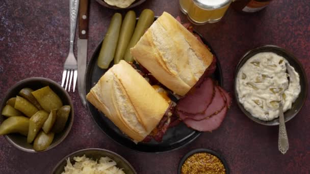 Deliciosos sanduíches de carne de pastrami servidos com copo de cerveja, picles, batatas fritas e lados. — Vídeo de Stock