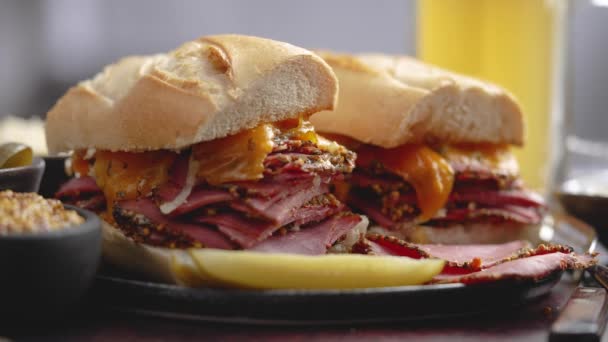 Deliciosos sándwiches de carne de pastrami servidos con un vaso de cerveza, encurtidos, papas fritas y acompañamientos. — Vídeos de Stock