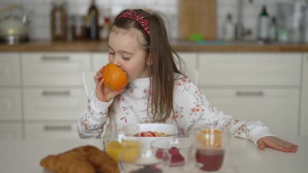 Flicka äter färsk apelsin under frukost — Stockvideo