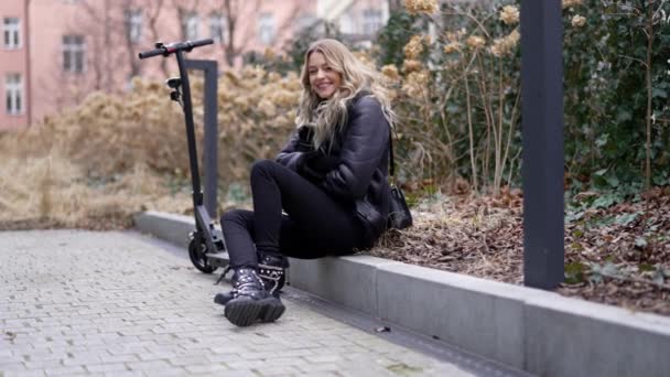 Mujer feliz con scooter eléctrico descansando en el parque de otoño — Vídeo de stock