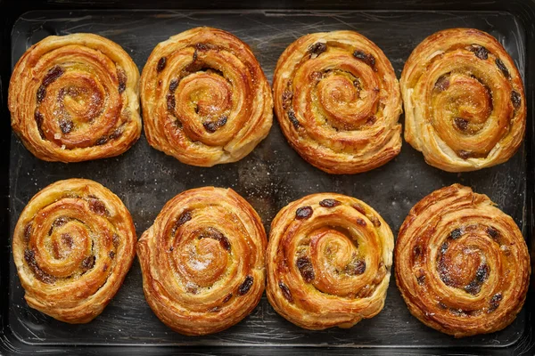 Rollos de canela de hojaldre caseros con pasas colocadas en la bandeja de hierro del horno —  Fotos de Stock