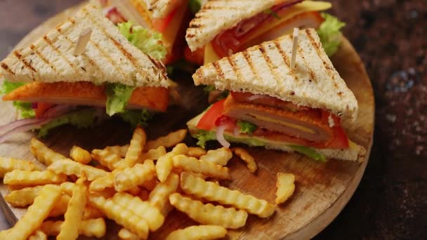 Σάντουιτς με κλαμπ σερβιρισμένα σε ξύλινη σανίδα. Με τηγανιτές πατάτες — Αρχείο Βίντεο