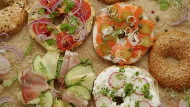 Saboroso colorido vários bagels com ingredientes saudáveis servidos em papel manteiga marrom — Vídeo de Stock