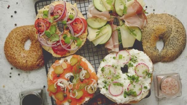 Deliciosos sándwiches de Bagel con queso cremoso, jamón, hummus, salmón y verduras — Vídeo de stock