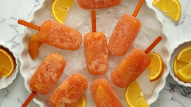 Zelfgemaakte, sappige, oranje ijslolly 's. Op een witte plaat met ijsblokjes — Stockvideo