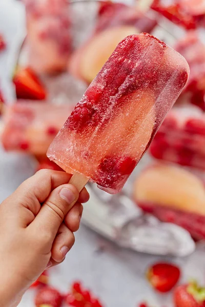 Close up on kids hand holding colorful red berry fruit popsicle. Healthy summer snack concept. — Stock Photo, Image