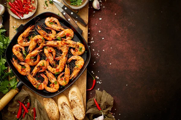 Goûteuses crevettes grillées appétissantes avec des épices sur la casserole avec des ingrédients sur fond rouillé — Photo