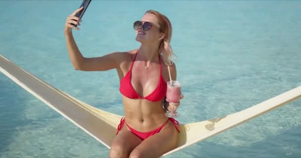 Female tourist drinking cocktail and taking selfie on hammock — Stock Video