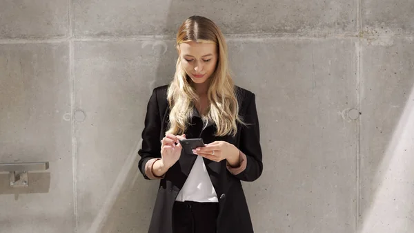 Businesswoman navegar por el teléfono celular cerca de la pared de hormigón —  Fotos de Stock