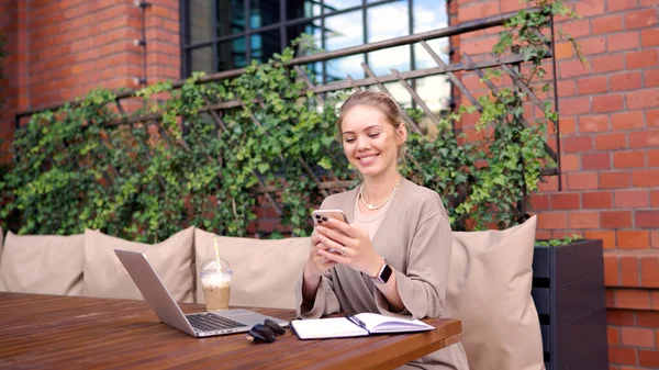 Happy freelancer käyttää älypuhelinta kahvilassa — kuvapankkivalokuva
