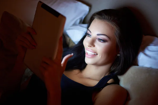 밤에는 태블릿을 읽고 침대에 웃는 여자 — 스톡 사진