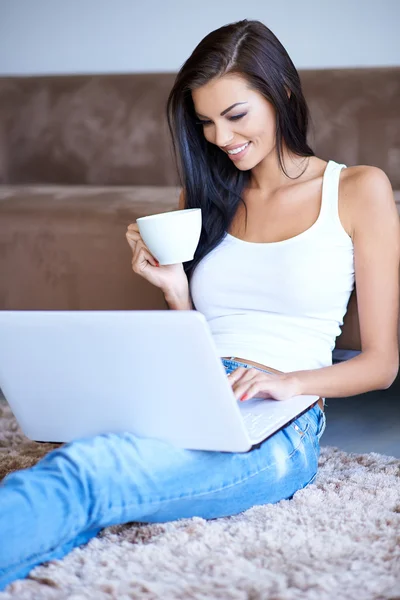 Frau trinkt Kaffee, während sie auf ihrem Laptop tippt — Stockfoto