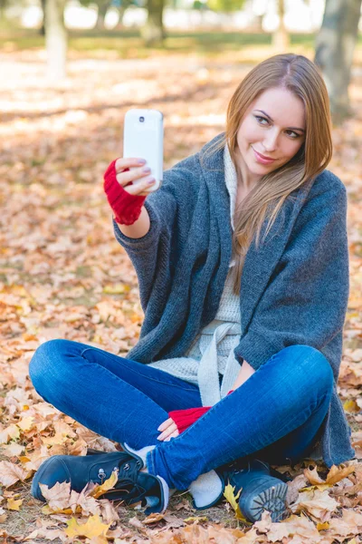 Hymyilevä nainen ottaa selfien syksyllä puistossa — kuvapankkivalokuva