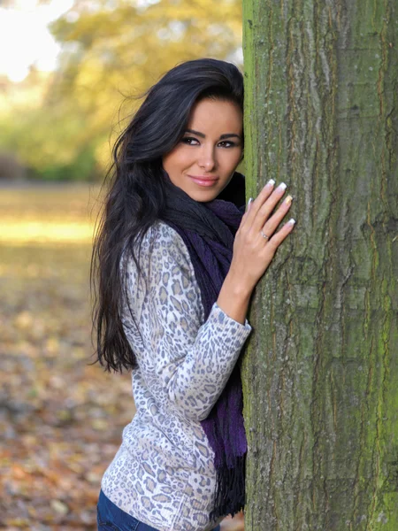 Усміхаючись досить молода жінка, спираючись на стовбур дерева — стокове фото