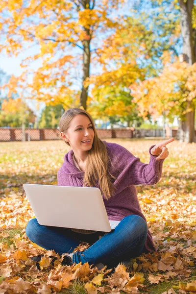 Mulher feliz sentada em folhas secas com laptop — Fotografia de Stock