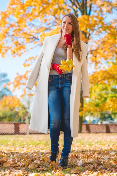 Kaunis nainen iso valkoinen takki tilalla lehdet — kuvapankkivalokuva