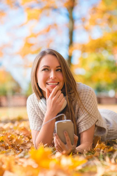 Pretty Lady Lying on Dry Leaves with Phone — Stock Photo, Image