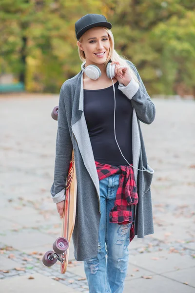 Žena s sluchátka držící Skateboard — Stock fotografie