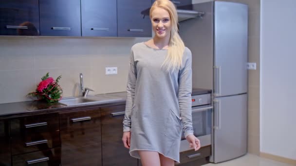 Blonde Frau im grauen Kleid steht in der Küche — Stockvideo