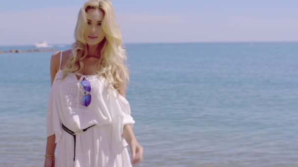 Блондинка жінка в сукні білим сонцем, стоячи на пляжі — стокове відео