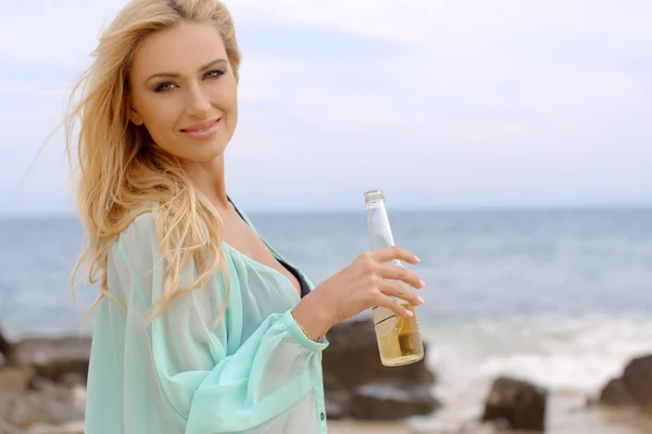 Mulher loira segurando garrafa de cerveja na praia — Fotografia de Stock