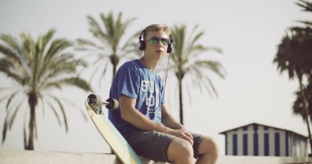 Chłopiec siedzący słuchania muzyki na zewnątrz — Wideo stockowe