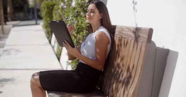 Lachende jonge vrouw met behulp van haar tablet buitenshuis — Stockvideo