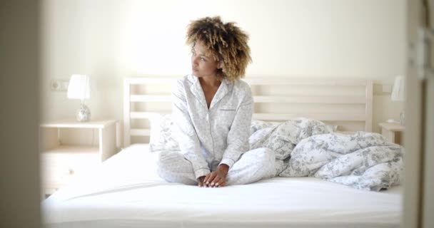 Женщина в пижаме сидит на кровати — стоковое видео