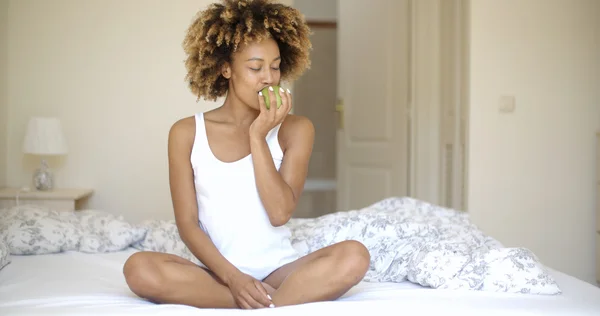 Женщина сидит на кровати и ест яблоко — стоковое фото