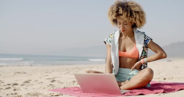 Женщина сидит на полотенце с ноутбуком на пляже — стоковое видео