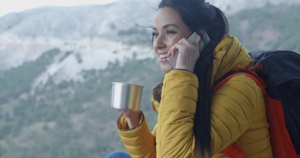 Woman drinking and talking on phone in mountains — 图库视频影像