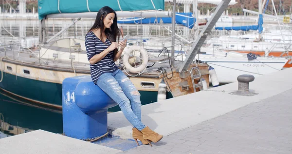 Woman sitting on quay and checking mobile — Stock fotografie