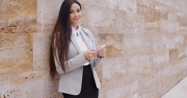 Businesswoman leaning wall and using phone — Stok fotoğraf