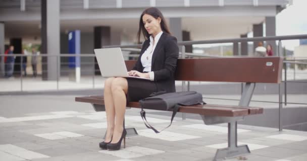 Mujer de negocios que trabaja en el ordenador portátil en el banco al aire libre — Vídeo de stock