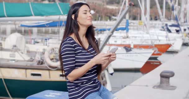Женщина сидит на пирсе и печатает смс — стоковое видео