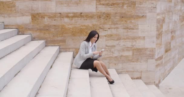 Mujer de negocios sentada en los escalones y usando el teléfono — Vídeo de stock