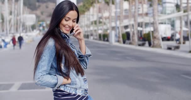Женщина сидит на пирсе и разговаривает по мобильному телефону — стоковое видео