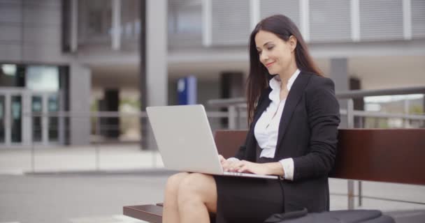 Mujer de negocios que trabaja en el ordenador portátil en el banco al aire libre — Vídeos de Stock
