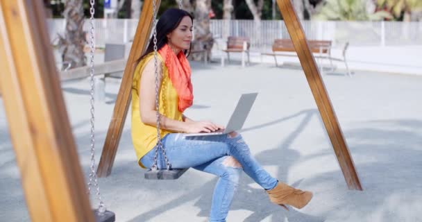 Woman sitting on swing and working on laptop — Stock Video