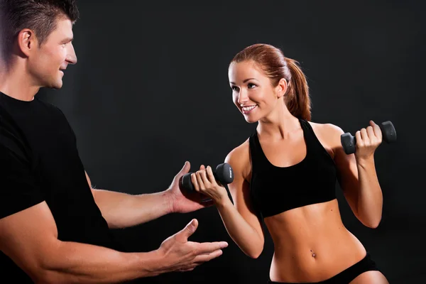 Young fit woman lifting dumbbells on dark background — Stock Photo, Image