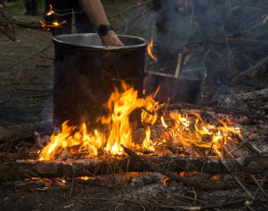 preparing food on a campfire with a large metal pot