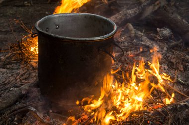 preparing food on a campfire with a large metal pot