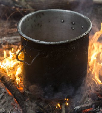 preparing food on a campfire with a large metal pot