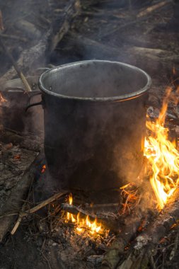 preparing food on a campfire with a large metal pot