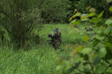 Bir grup maskeli insan ormanda paintball oynuyor.
